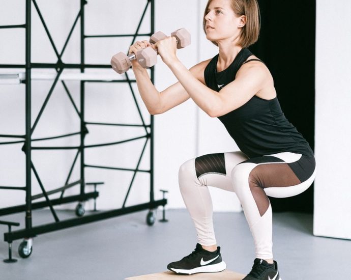 A woman in sportswear performs a squat with dumbbells indoors, embodying strength and healthy living.